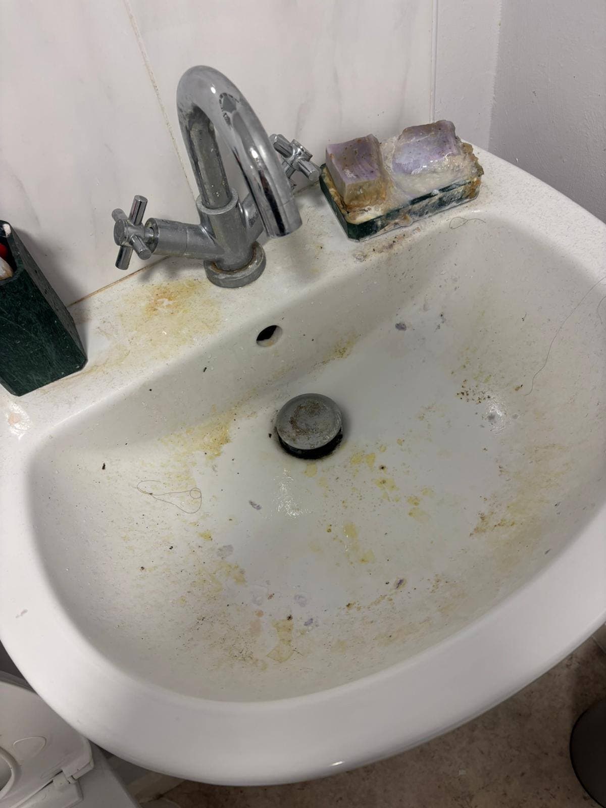 White bathroom basin streaked with yellow grime and a dull, dirty chrome tap before cleaning